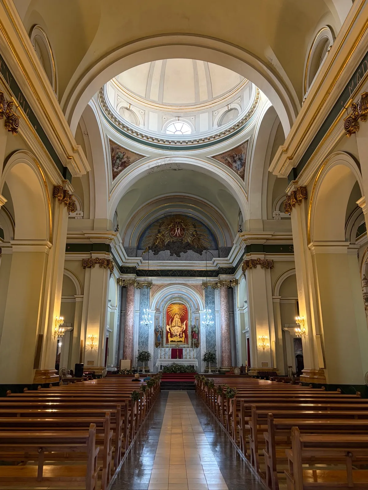 Inside the church: the aisle between wooden pews leads to the altar, with a statue of the Virgin in a red niche between marble columns
