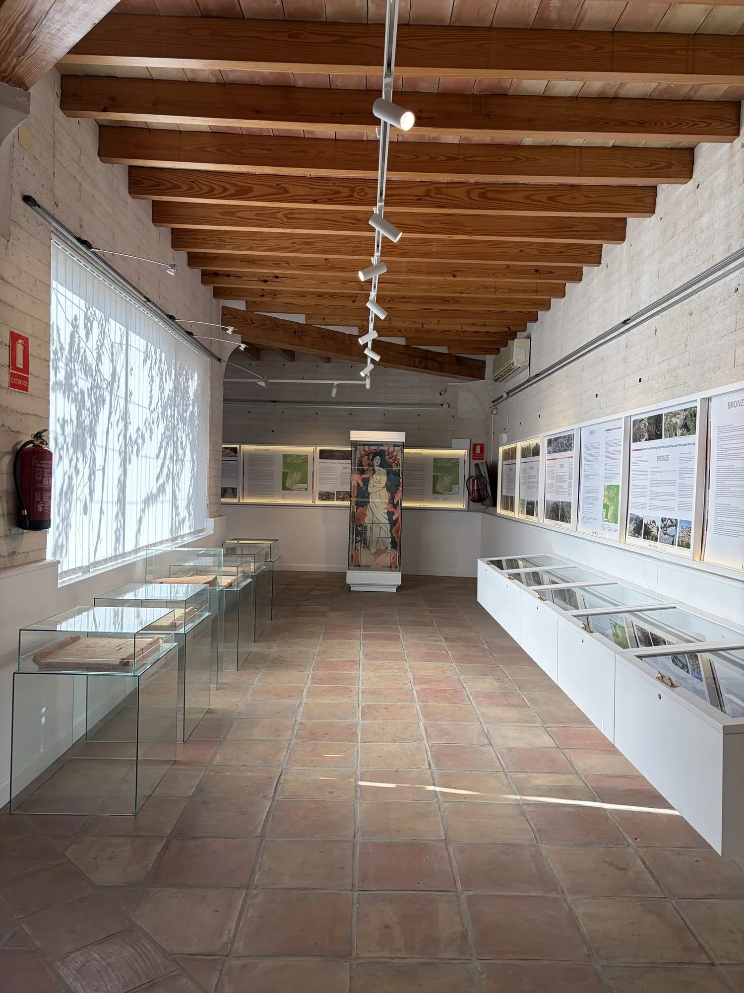 Archaeology room with glass cases along both walls and panels on the Iberians, the Bronze Age, and Christians and Muslims