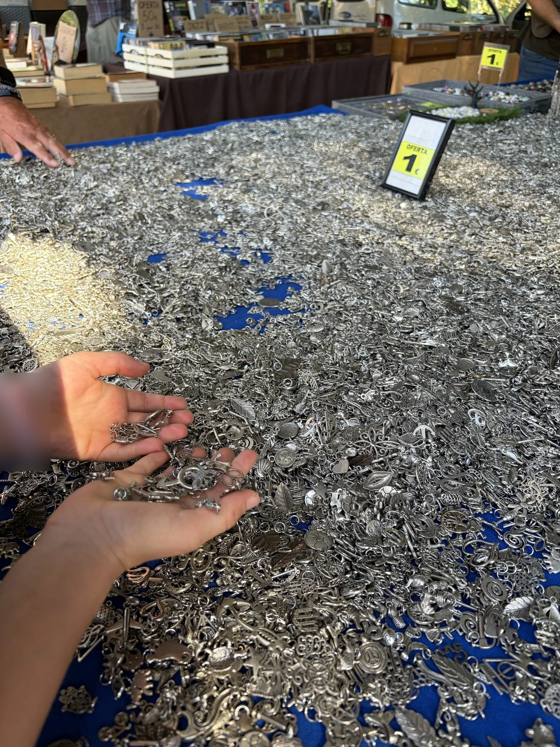 A child's hands full of silver charms at the big charms table, with a €1 offer sign