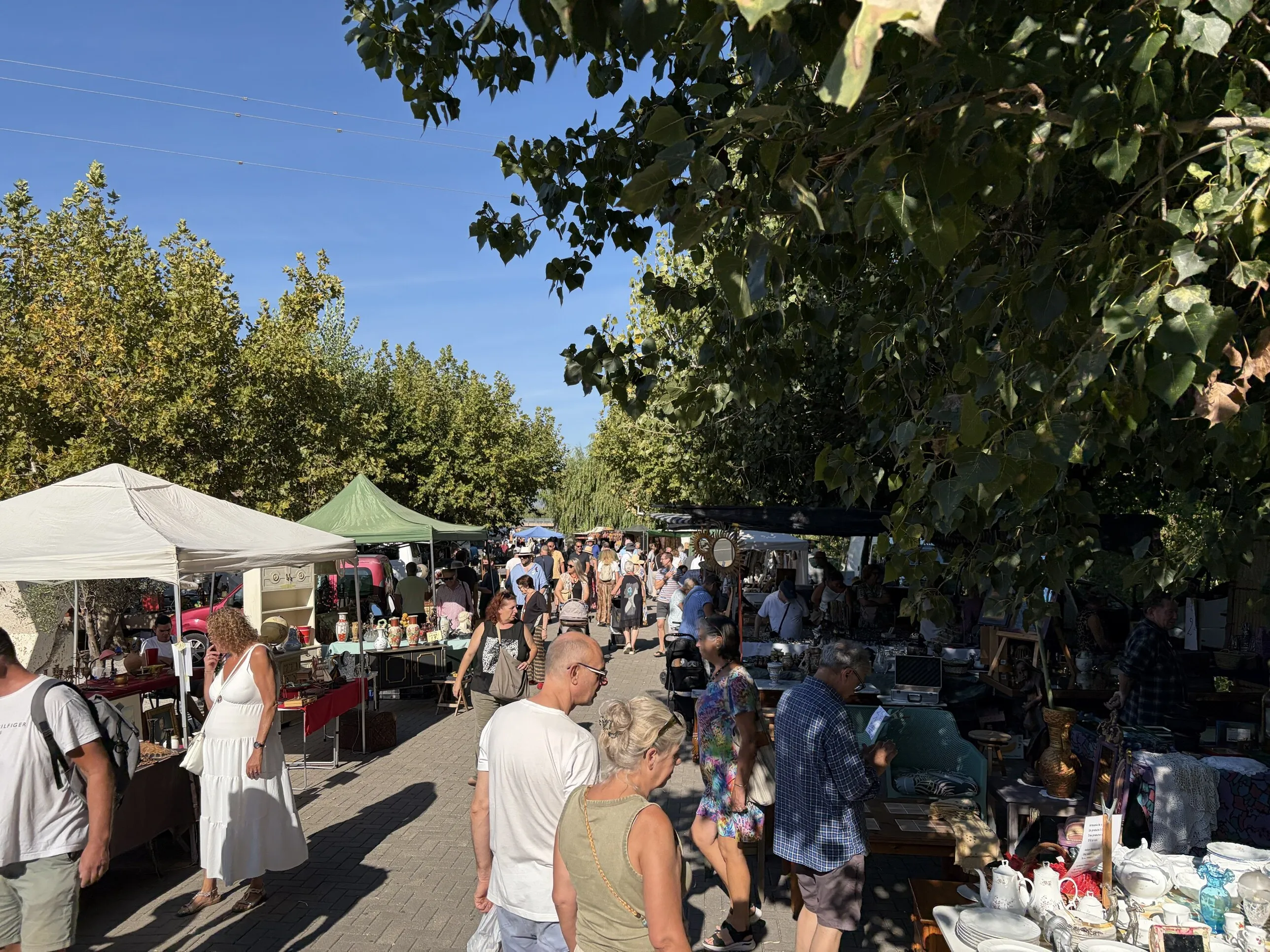 Shoppers walking between flea-market stalls with vases, china and old furniture in the Saturday sun